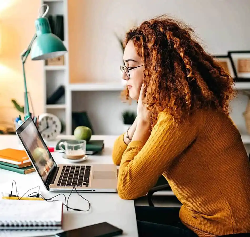 female student wearing an orange sweater, at a laptop