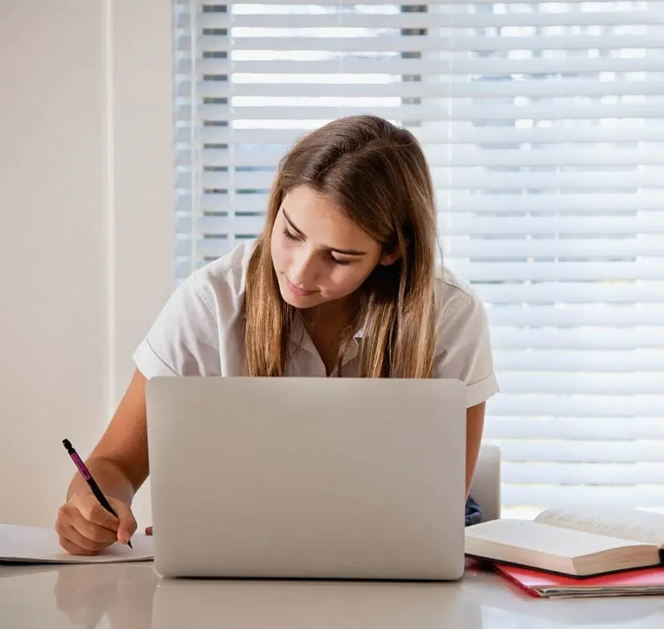 Female student writing while using laptop