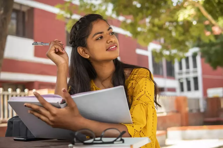 female student pensively smiling, studying outside