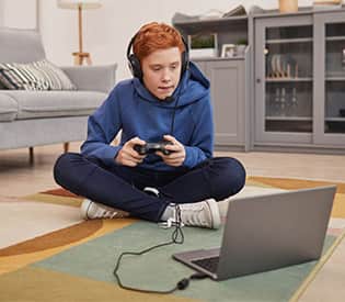 Middle school boy in blue hoodie playing video games on a laptop