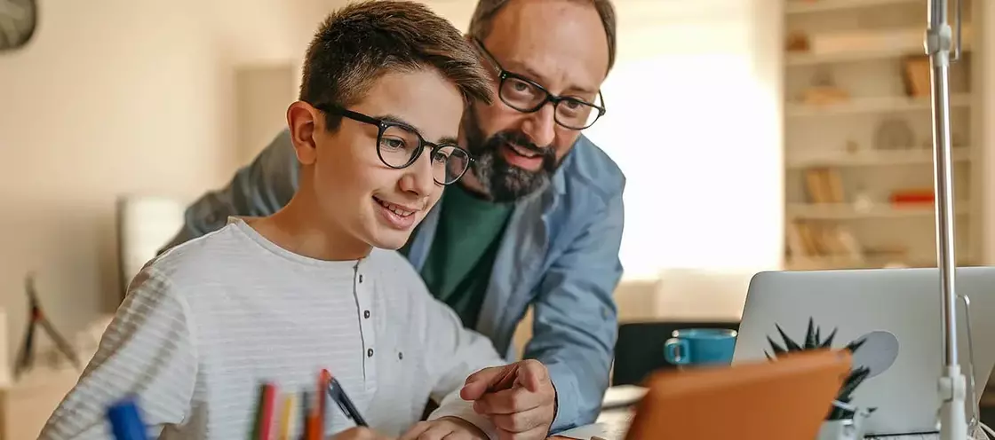 Dad teaching son, pointing over shoulder at laptop