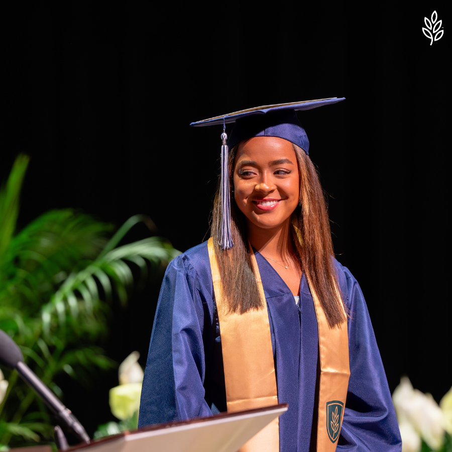 Girl with brown hair smiling in a blue graduation cap on stage