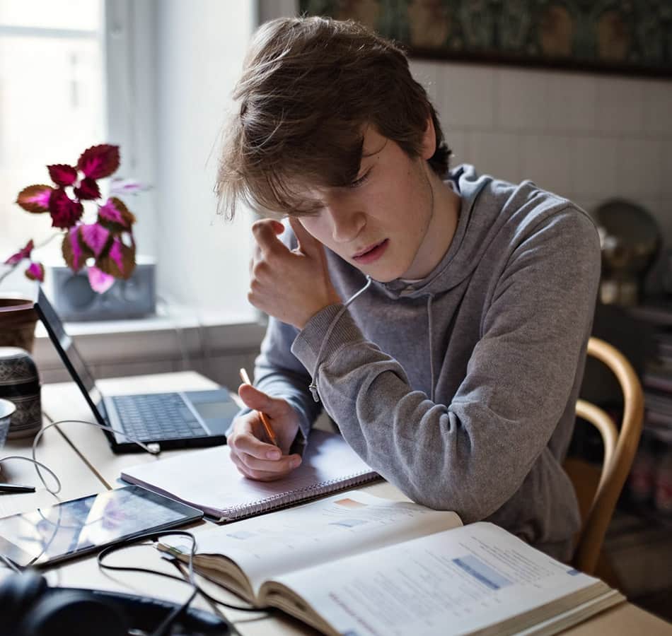 male teenager taking notes while taking online class