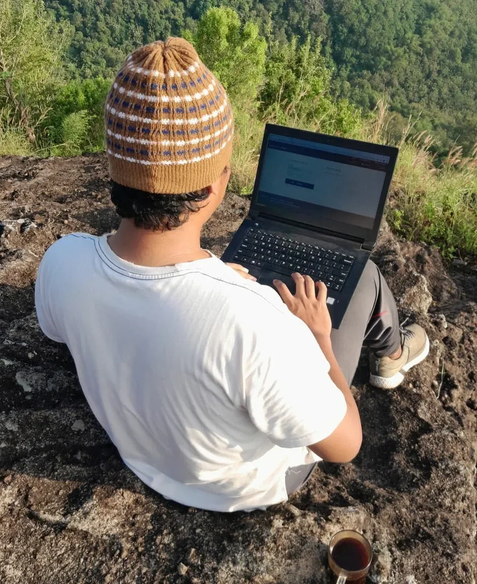 student on a mountaintop using his laptop