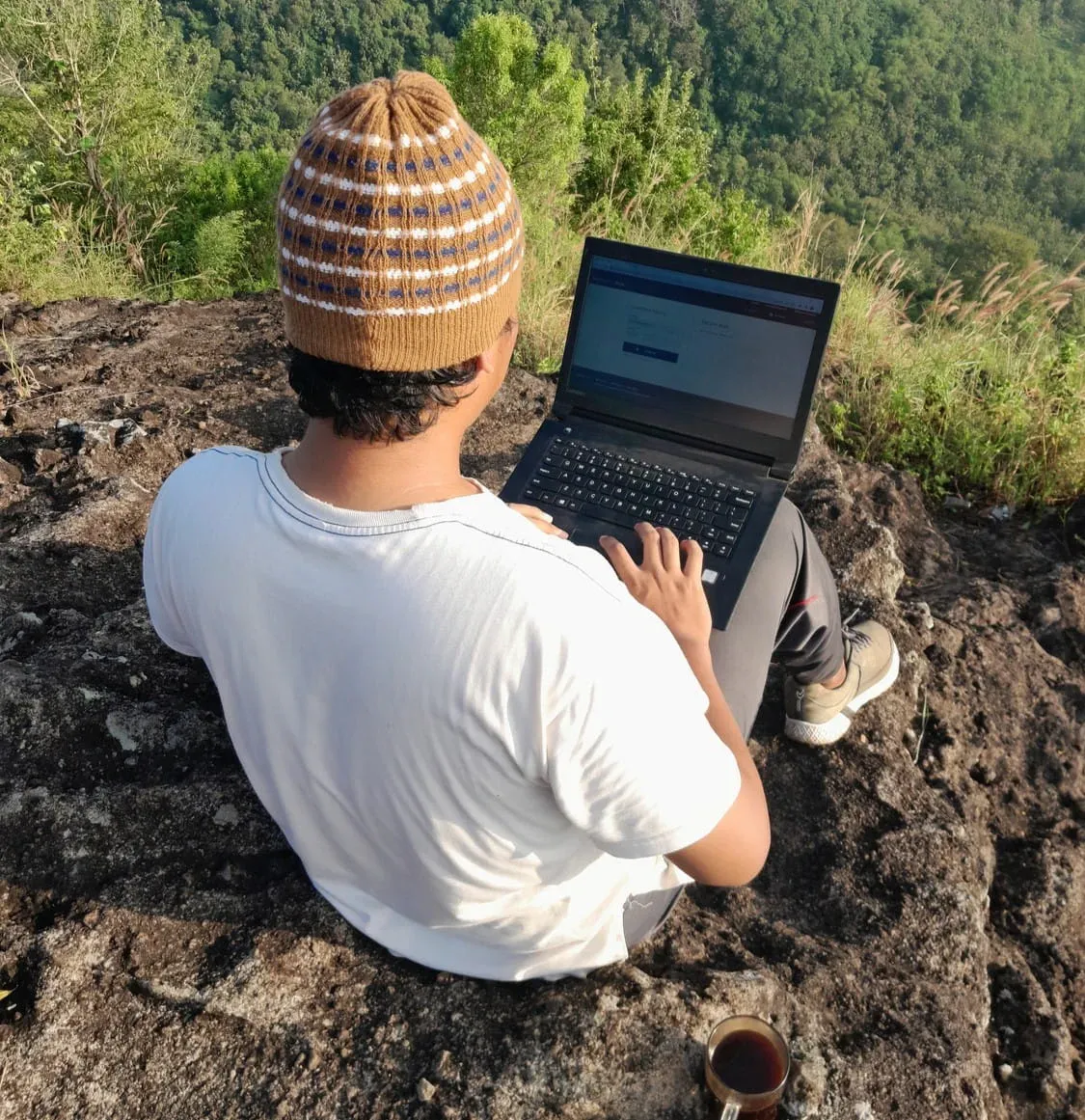 student on a mountaintop using his laptop