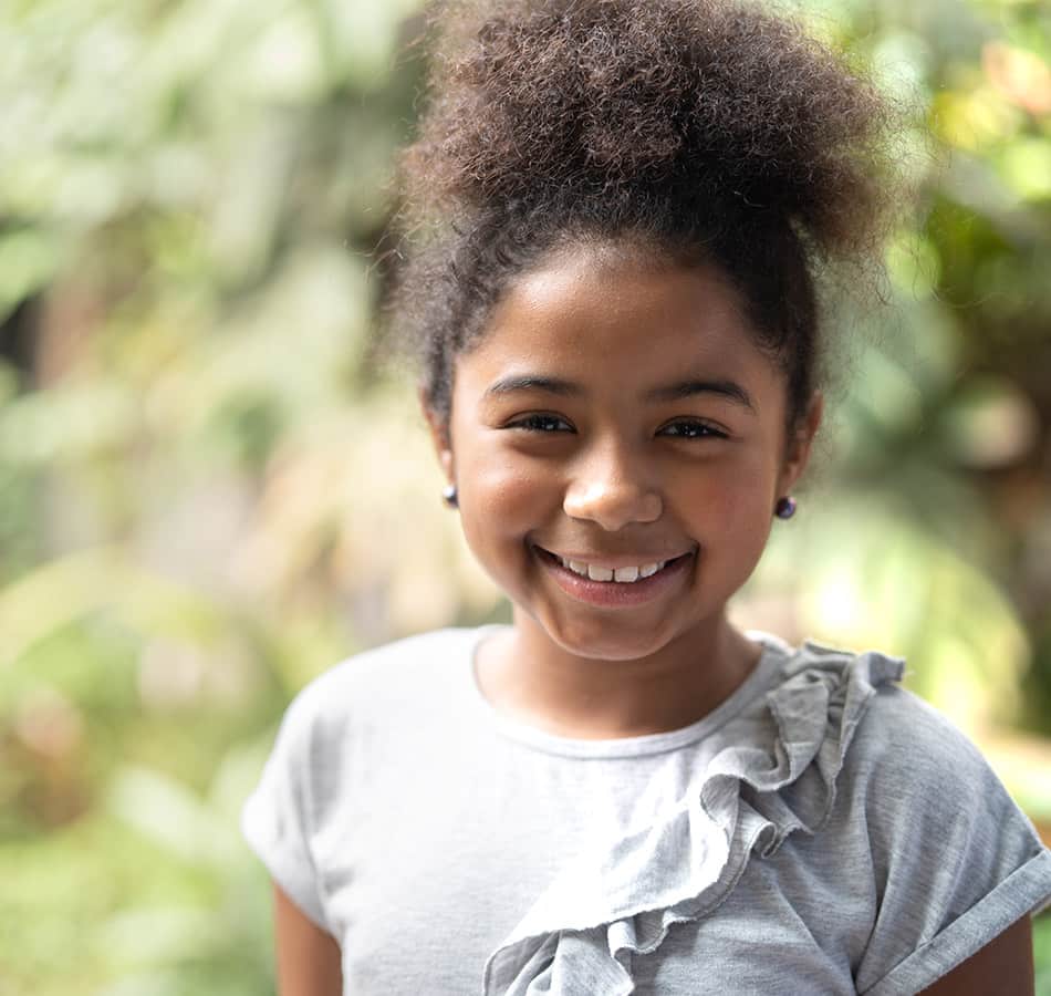 girl smiling at the camera, blurry foliage behind