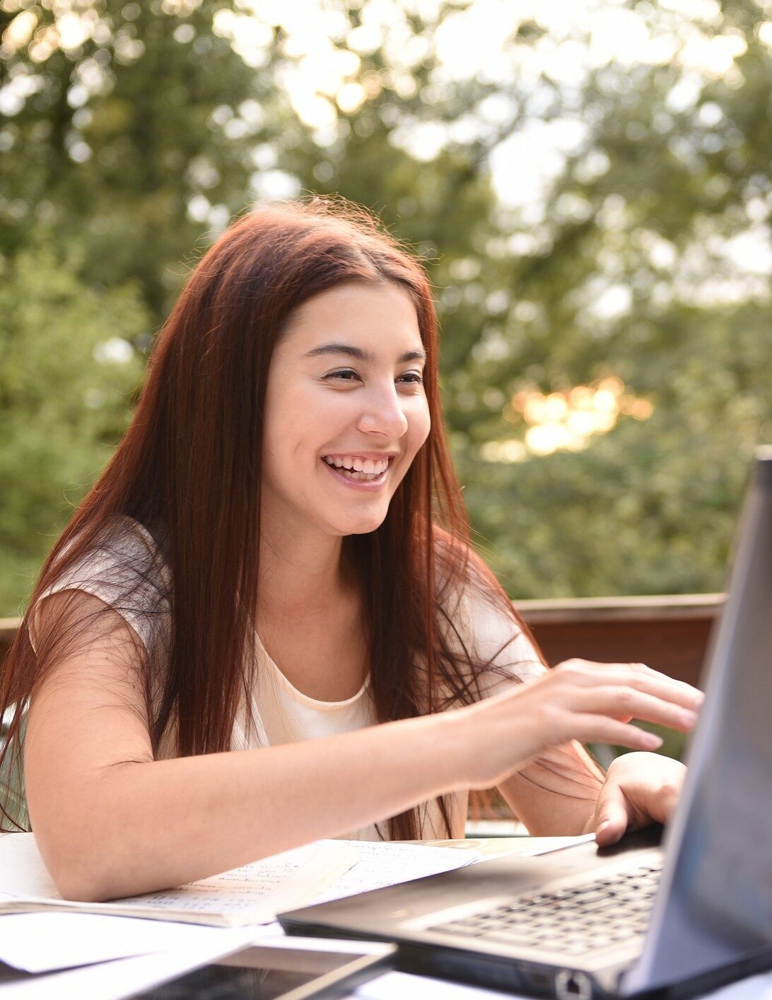 Young woman with red hair smiling outside typing on a computer